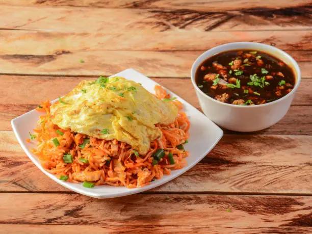 Triple Schezwan Fried Rice is a lip smacking complete meal combination of Rice, chicken,egg and crispy fried noodles served with spicy and fragrant schezwan gravy, Indian cuisine, selective focus