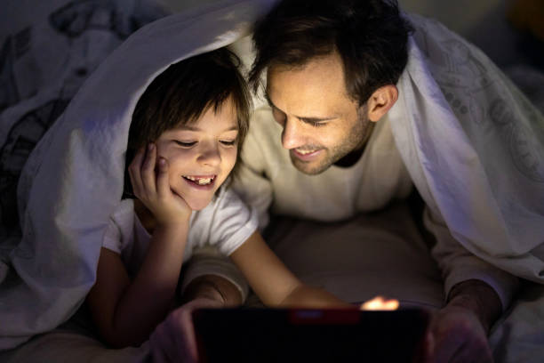 istock Little boy and his father using digital tablet together at night in bed 1292617195