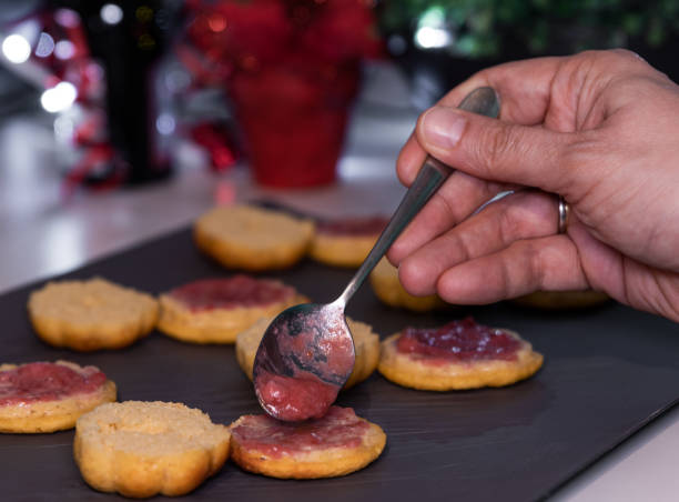 Woman's hand pouring with silver spoon home freshly made strawberry fruit jam on home baked little cake on kitchen counter with Christmas holidays decoration. Soft focus background, bokeh la mano de la mujer vierte con cuchara de plata casero recién hecho mermelada de fruta de fresa en el pequeño pastel horneado en casa en el mostrador de la cocina con la decoración de las vacaciones de navidad. fondo de enfoque suave, bokeh