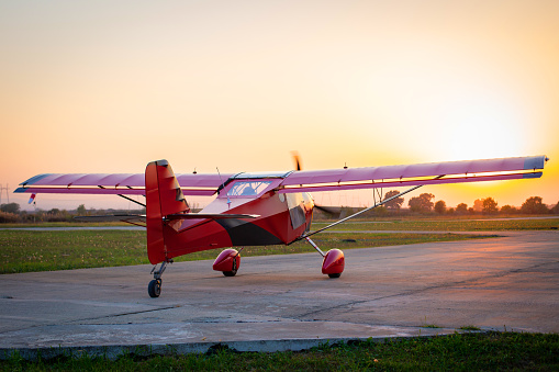 Small private lightweight propeller airplane against the sunset. Red aircraft on the runway.