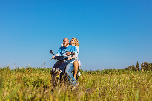 A beautiful blonde Dutch woman and redhead man at a typical dutch countryside on a scooter