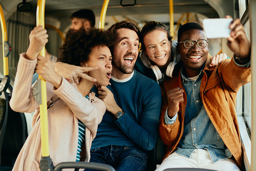 Group of happy friends having fun while traveling by bus and talking selfie with mobile phone.