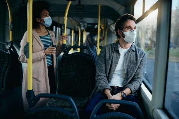 Pensive man with face mask commuting by bus and looking through the window. Man with protective face mask thinking of something while traveling by public transport and looking through the window. public transportation stock pictures, royalty-free photos & images