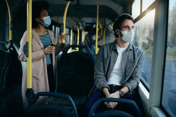 Photo of Pensive man with face mask commuting by bus and looking through the window.