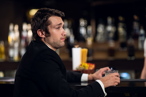 a bored young man is sitting at the bar with a cocktail in his hands.