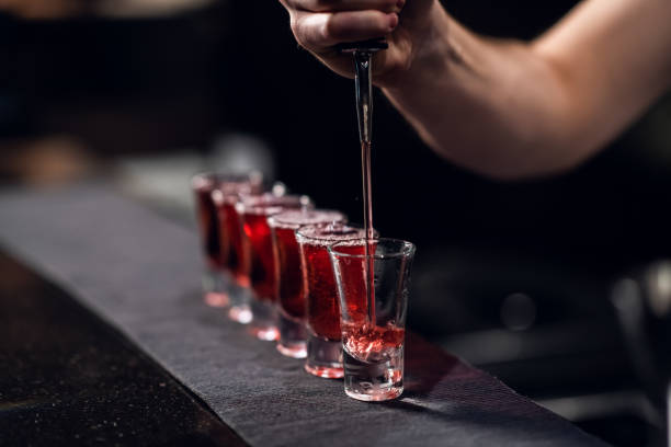 the bartender fills shots with red liquor from a bottle on the bar - hard liqueur imagens e fotografias de stock