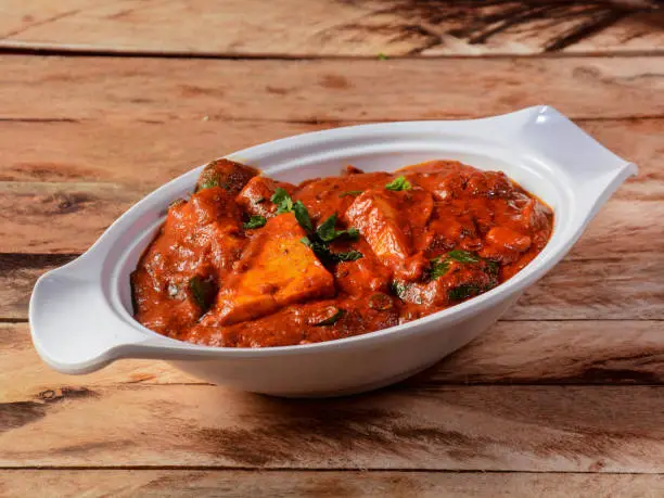 Paneer Tikka Masala is a famous indian dish, served over a rustic wooden background, selective focus