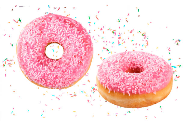 istock Delicious donuts decorated with pink chocolate icing and sugar sprinkles fall through the air with colored sprinkles on a white background 1292630017