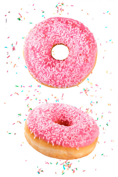 istock Vertical composition of delicious doughnuts decorated with pink chocolate icing and sugar sprinkles falling through the air with isolated colored sprinkles on a white background 1292630018