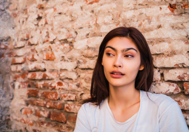 Attractive woman looking aside at a spider web inside an alcove in an exterior red brick wall in a close up portrait