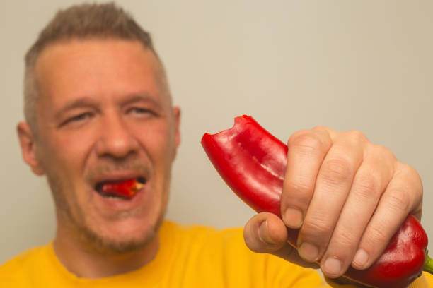 Adult man eating raw fresh red pepper
