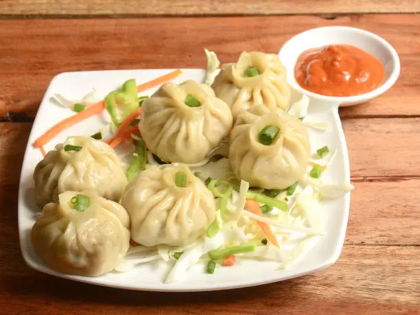 Photo of Veg steam momo. Nepalese Traditional dish Momo stuffed with vegetables and then cooked and served with sauce over a rustic wooden background, selective focus