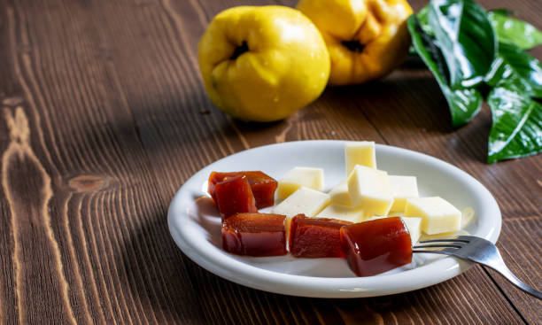 白いプレートに自家製のクインスジャムとチーズのスライス、木製のテーブルの上に新鮮な熟したクインスフルーツ。典型的な伝統的なスペインのデザート。 - quince ストックフォトと画像