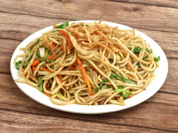 Photo of Veg Hakka Noodles a popular oriental dish made with noodles and vegetables, served over a rustic wooden background, selective focus