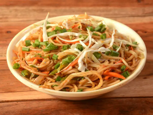 Photo of Veg Hakka Noodles a popular oriental dish made with noodles and vegetables, served over a rustic wooden background, selective focus