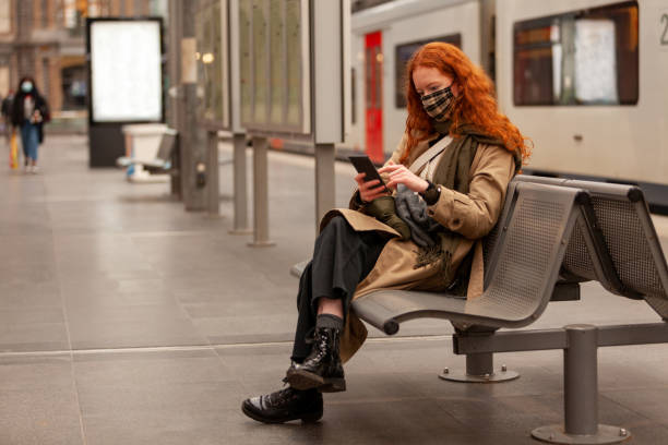While waiting for her commuter train to arrive a young curly red haired student swipes on het mobile phone stock photo