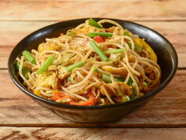 Photo of Chicken chow mein a popular oriental dish with noodles and vegetables, served over a rustic wooden background, selective focus