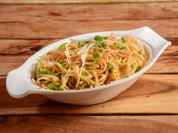 Photo of Veg Hakka Noodles a popular oriental dish made with noodles and vegetables, served over a rustic wooden background, selective focus