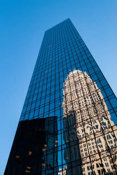 Photo of Large reflective skyscraper in downtown city reflecting the blue sky and another huge building in its glass windows