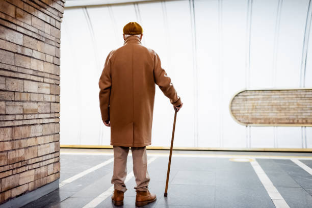 back view of aged man in autumn outfit standing with walking stick on underground platform back view of aged man in autumn outfit standing with walking stick on underground platform flat cap stock pictures, royalty-free photos & images