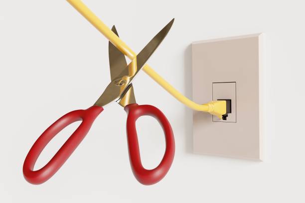 A pair or red scissors about to snip an ethernet cable connected to the wall