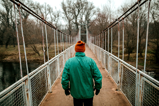 Senior walking in nature, he is crossing metal bridge on the river.