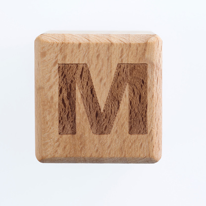 Wooden block with letter M on white background.