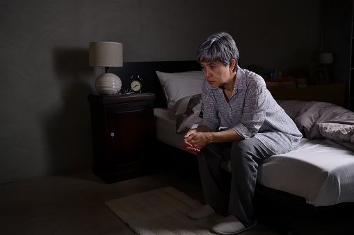 Depressed senior woman sitting in bed cannot sleep from insomnia