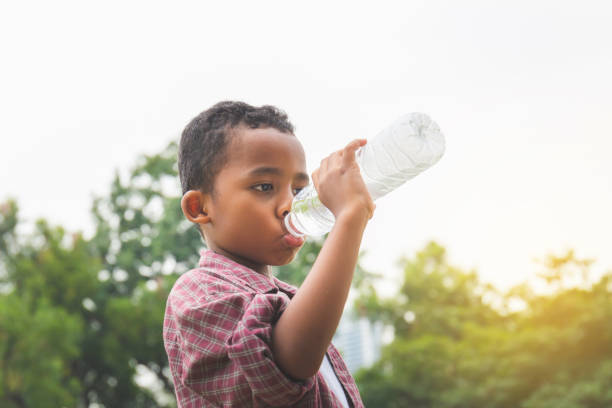 eau potable africaine gaie de garçon après avoir joué au stationnement - water child bottle little boys photos et images de collection