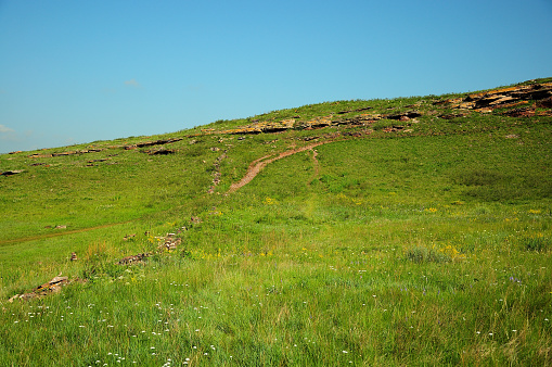 A path overlooking the top of a hill with the remains of an ancient stone wall. Mountain Range Chests, Khakassia, South Siberia, Russia.