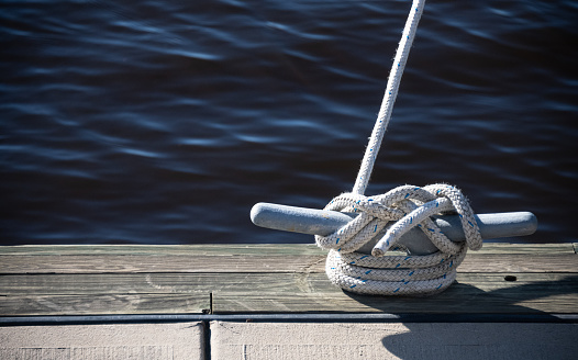 A boat is anchored to a cleat hitch in a coastal harbor.