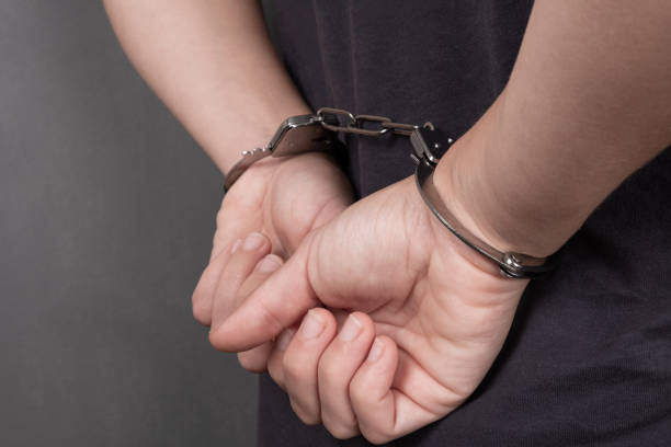aresztowana osoba w kajdankach na ciemnym tle z bliska, przykuta rękami na plecach - freedom legal system handcuffs security zdjęcia i obrazy z banku zdjęć