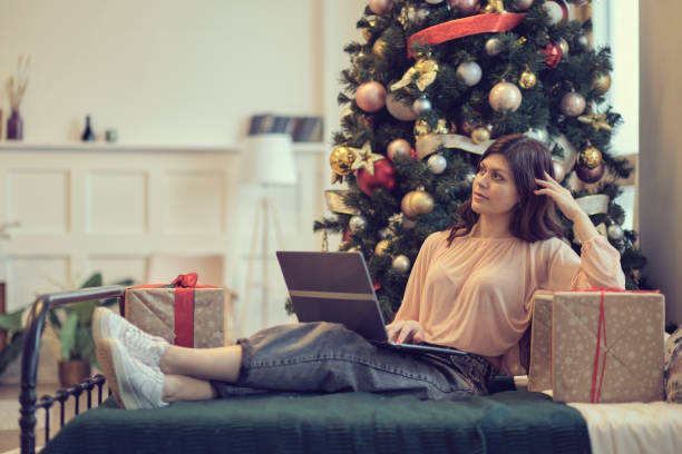 istock Young woman lying under decorated pine tree among gift boxes and packages in home interior. Christmas shopping online, sales and discounts promotions during winter holidays, lockdown coronavirus 1292681116