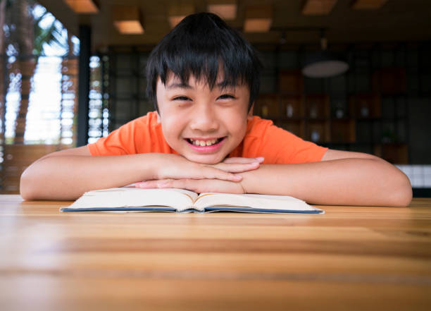 Boy smiling with a book on wooden table.  Learning at home stock photo