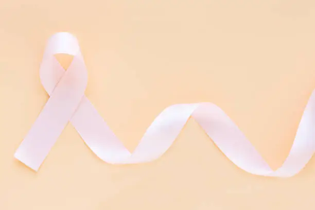 Peach color ribbon curl on pastel orange or beige color background with copy space, symbol for Uterine and Endometrial cancer awareness, World Cancer Day. Healthcare or hospital and insurance concept.