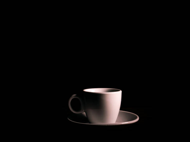 istock White ceramic coffee cup with saucer on a black background. 1292684812