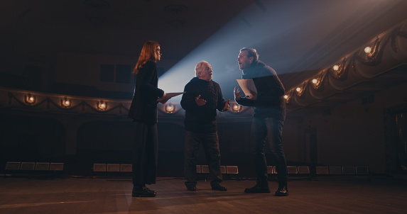 Senior director helping man and woman to act out argument scene during rehearsal on stage in theater
