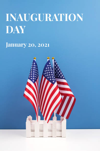 istock Vertical composition with USA flags on white table against blue wall background, copyspace for your text. Inauguration Day 2021 concept 1292691415