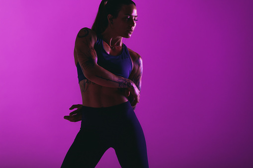 Monochrome portrait of female athlete doing workout. Fit woman doing fitness training on purple background.