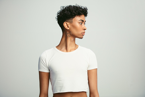 Man wearing crop top and earring looking away. Young androgynous man wearing earring against white background.