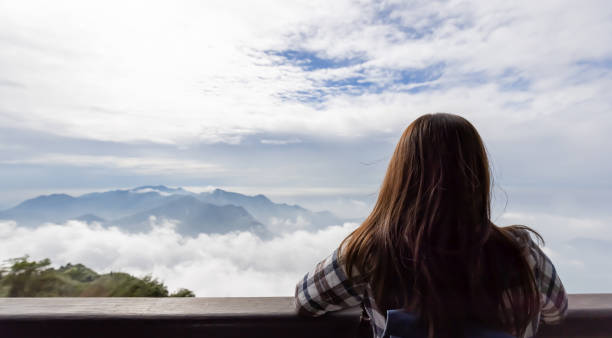 back view of asian young woman traveler looking at cloud over the mountain
