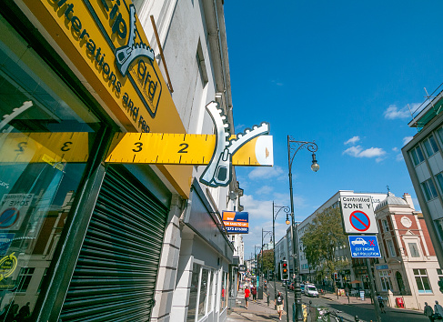 People walking on the sidewalk past The Zipyard on Queens Road in Brighton, England, which specialises in clothing alterations