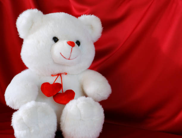 istock White Teddy bear with red hearts on a red cloth background. 1292700038