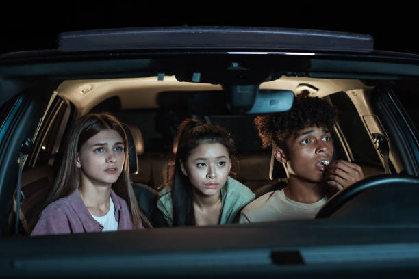 portrait of diverse young friends looking emotional, while sitting together in the car and watching a movie in a drive in theater - drive in movie car inside of billboard imagens e fotografias de stock