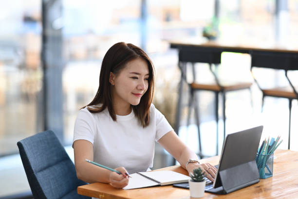 istock Rear view of smiling female designer working with computer tablet and making some note on notebook at office room. 1292702205