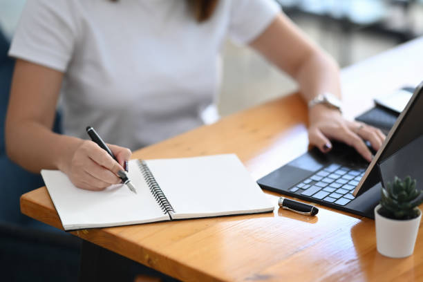 istock Close up view of female using computer tablet and making notes or planning schedule in notebook. 1292702207