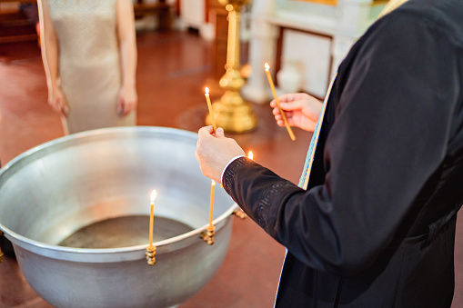 a priest holds candles in his hands near the baptismal font.