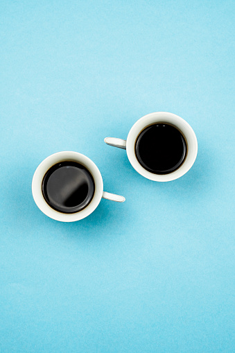 Two coffee cups on bright blue background. Vertical shot of two coffee mugs from above