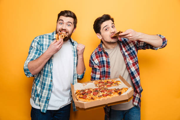 Two cheerful men in shirts eating pizza stock photo
