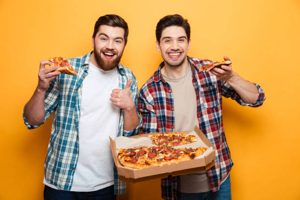 istock Two joyful men holding pizza and looking at the camera 1292711497